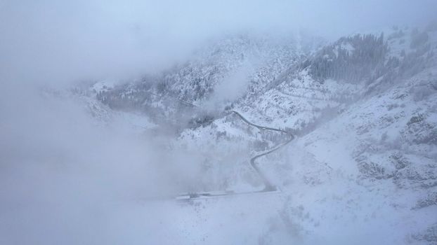 Snowy mountains with coniferous trees in the clouds. Medeo Dam. Everything is in fog and snow. Christmas and New Year have come. Aerial view from the drone on road, dam and trees. Almaty, Kazakhstan