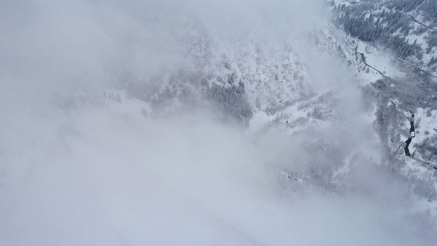 Snowy mountains with coniferous trees in the clouds. Medeo Dam. Everything is in fog and snow. Christmas and New Year have come. Aerial view from the drone on road, dam and trees. Almaty, Kazakhstan