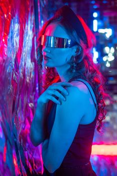 Close-up portrait of caucasian woman in sunglasses in neon light against foil wall