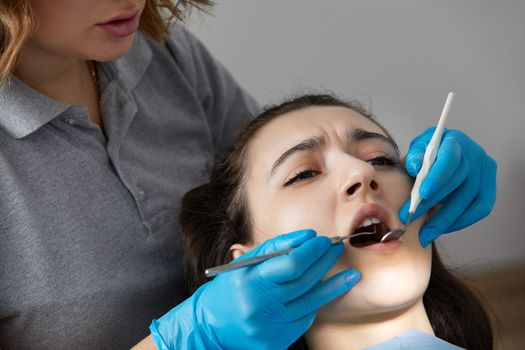 Dentist checking teeth of a patient with dental mirror. Woman having teeth examined at dentists