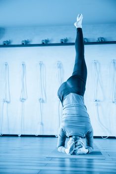 Handsome woman having yoga practice and standing on head in white lit room. Concept of physical and mental health, happy living and well being.