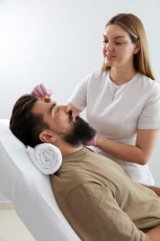 Cosmetologist applying a clay mask to male face. Spa treatment and face care in the beauty salon for men