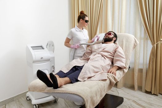 Bearded man getting laser facial treatment by professional cosmetologist in a beauty clinic. Healthy man lifestyle concept