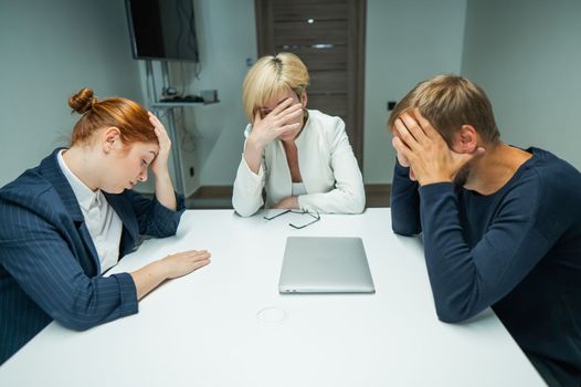 Blond, red-haired woman and bearded man in suits in the office.Colleagues sit at a table in a conference room and hold their heads in thought