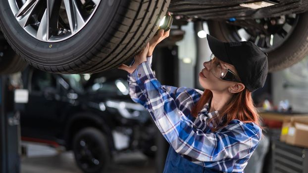 A female mechanic inspects a raised car. A girl at a man's work