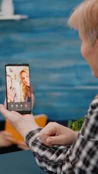 Senior woman having video call online talk with nephew using smartphone sitting in living room. Retired granny using modern internet online tech to connect with grandparents