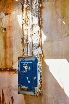Image of Abandoned plaster wall detail with blue peeling painted power box in sunspot
