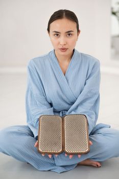 Asian woman sitting in lotus position on yoga mat and holding sadhu boards