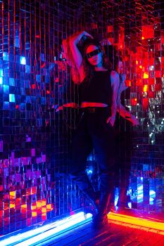 Portrait of a caucasian woman in sunglasses in neon light against a mirror wall