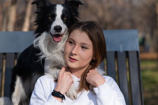 Caucasian woman hugging her dog Border Collie while sitting on a bench in autumn park