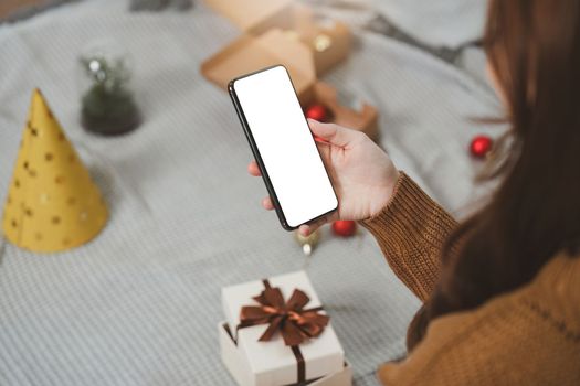 Cheerful lady using smartphone with gift box. Marry Christmas and Happy Holidays and New Year eve celebrating concept.