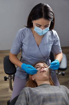Dentist checking teeth of a patient with dental mirror. Woman having teeth examined at dentists