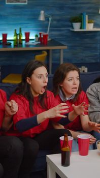 Mixed race group of people watching at football game on television cheering sport team after winning championship. Excited friends celebrating match competition while sitting on sofa late at night