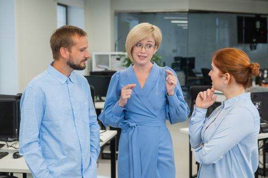 Colleagues communicate at work. Red-haired woman, blonde and bearded man in a denim shirt in the office