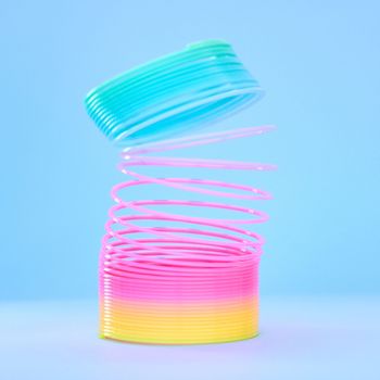 Rainbow slinky toy, spring and plastic product in studio isolated against a blue background mockup. Flexible toys, colorful spirals and childhood item stretched out for playing, having fun and games