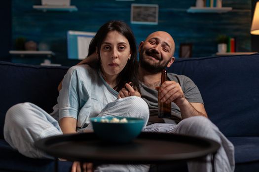 POV of man and woman laughing and watching film on TV, having fun with comedy movie on television channel program. Cheerful happy couple enjoying broadcast show for entertainment.