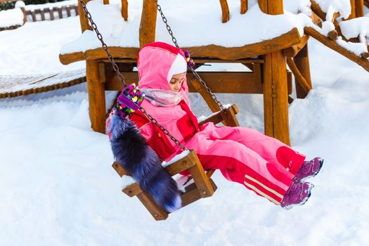 Charming little girl on swing in snowy winter.