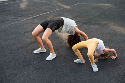 A little girl and her mom do a bridge exercise at the outdoor sports ground