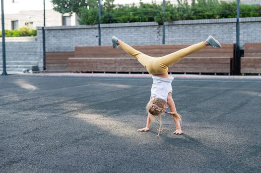 Caucasian girl makes a cartwheel on the sports field outdoors