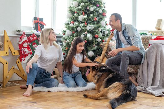 smiling family and daughter with dog sitting near christmas tree with gifts.