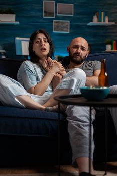 POV of man and woman watching scary horror movie on television, feeling terrified and sad. Anxious couple looking at film on TV channel program, being afraid, scared, shocked at home.