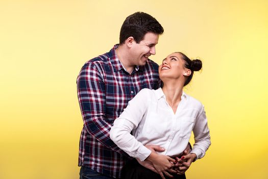 Woman looking with love at her husband on yellow background in studio