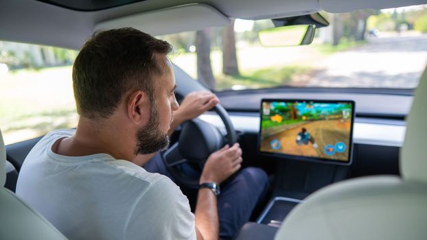 Novosibirsk, Russia - 10.08.2022: Caucasian man playing games while driving tesla car