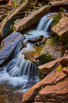 Image of Detail of pair of small cascading waterfalls pouring over mossy boulders in creek