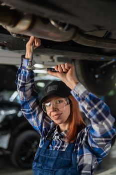 Female mechanic unscrew the nuts on the bottom of the car that is on the lift. A girl at a man's work