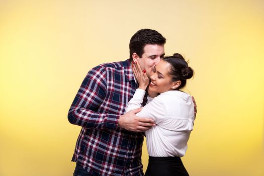 Man kissing her wife on the cheek in studio on yellow background