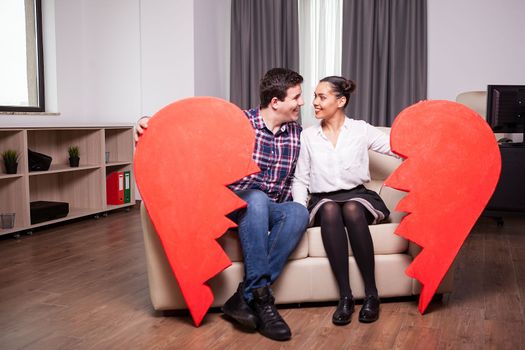 Couple looking at each other while holding two part of one big red heart