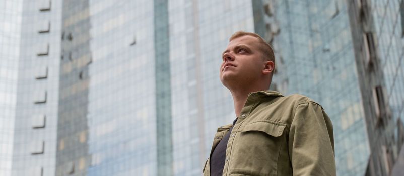 A pensive man stands against the backdrop of a skyscraper