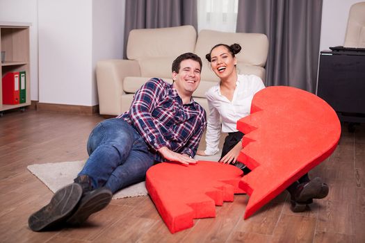 Laughing couple with two pieces of one big heart in the living room