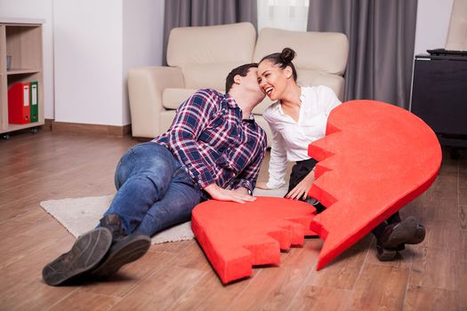 Laughing couple with two pieces of one big heart in the living room