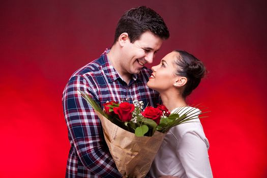 Couple on a date while woman holds flowers in hands. Red background and studio photo