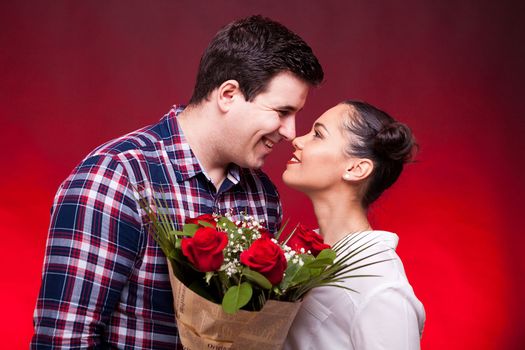 Inlove couple looking at each other. Woman is holding a roses bouquet in hands on red background in studio photo