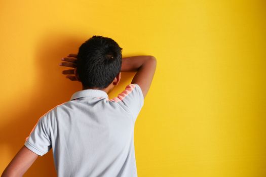 sad teenage boy covering his face on yellow background .