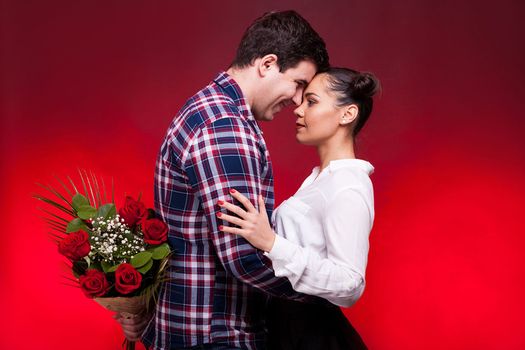 Man with a roses bouquet at his back on a first date with a beautiful woman. Red background and studio photo