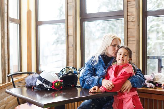 Cheerful mother with daughter on skiing sitting in cafe on ski terrain
