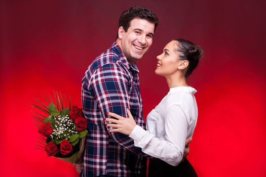 Man with a roses bouquet at his back on a first date. Red background and studio photo