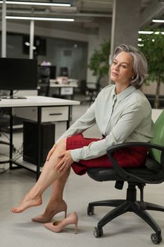 Caucasian woman massaging her tired legs while sitting in the office