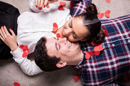 Happy man and woman lying on the floor covered with small red hearts