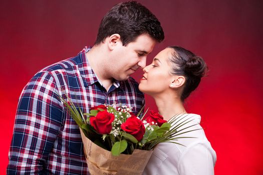 Beautiful couple with a roses bouquet in hands on red background