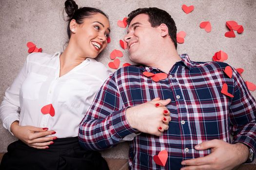 Couple looking at each other while lying on the floor next to small red hearts