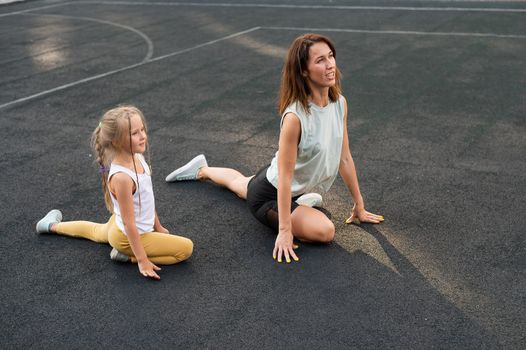 Mother and daughter go in for sports outdoors. Caucasian woman and little girl are engaged in fitness at the stadium