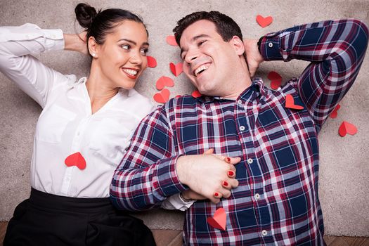 Happy couple lying on the floor next to small red papper hearts