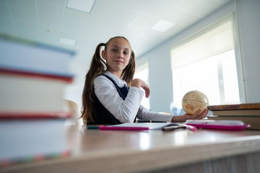 Caucasian schoolgirl sits at her desk at school and studies the globe