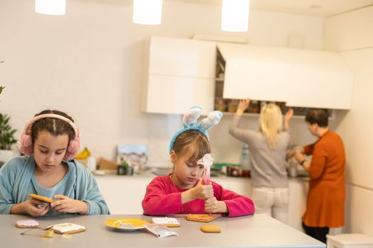 Two girls decorate cookies on plates with chocolate icing. Cooking treats for halloween celebration.