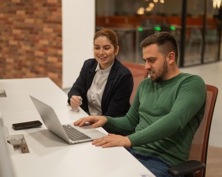 Caucasian bearded man and red-haired woman work in a modern coworking space. Colleagues discuss work