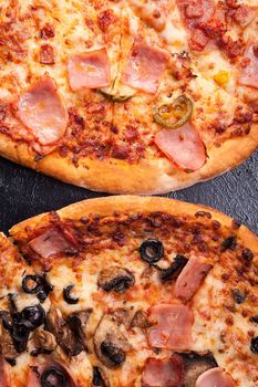 Top view of two pizza lying next to each other on dark wooden background